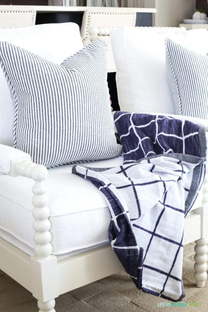 White spindle chair with navy blue and white windowpane throw and striped pillow.