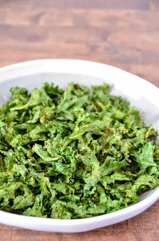 A white bowl of air fried kale chips on the table.
