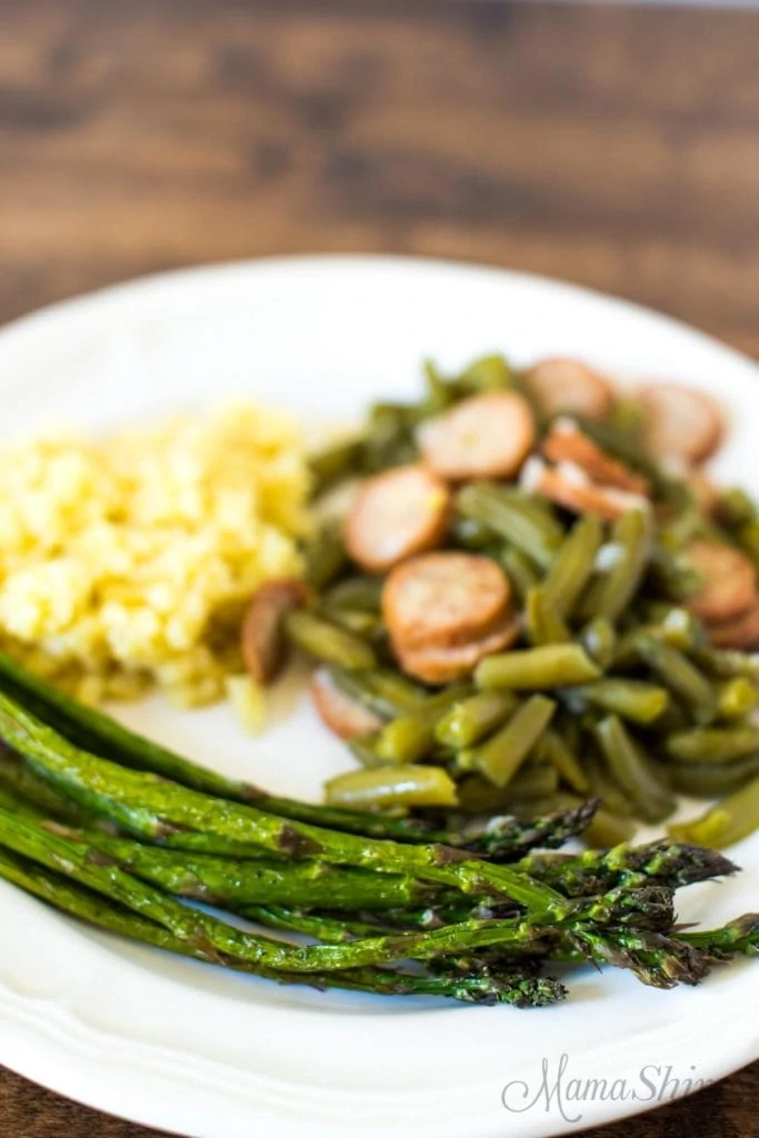 Air fried asparagus on a white plate with green beans and rice.