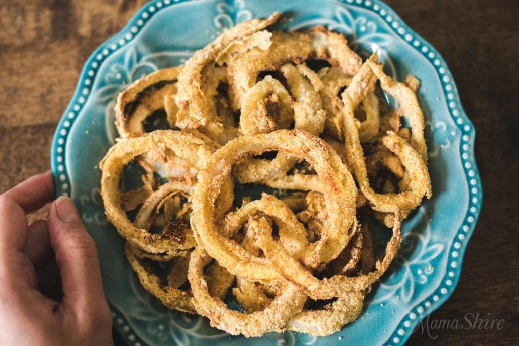A blue ornate bowl with fried onion rings in it.