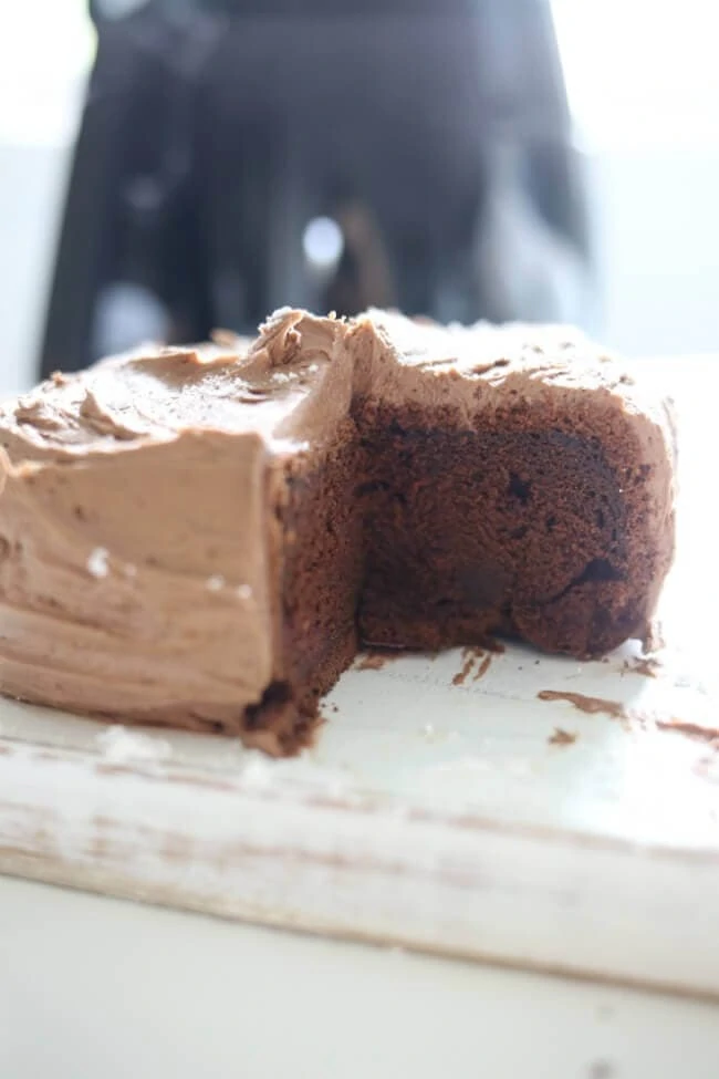 A chocolate cake that is iced with a piece taken out of it.