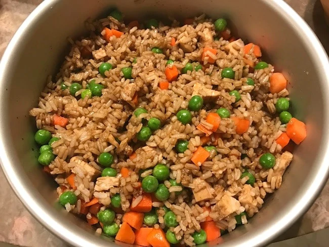 A bowl of chicken fried rice with peas and carrots in it.