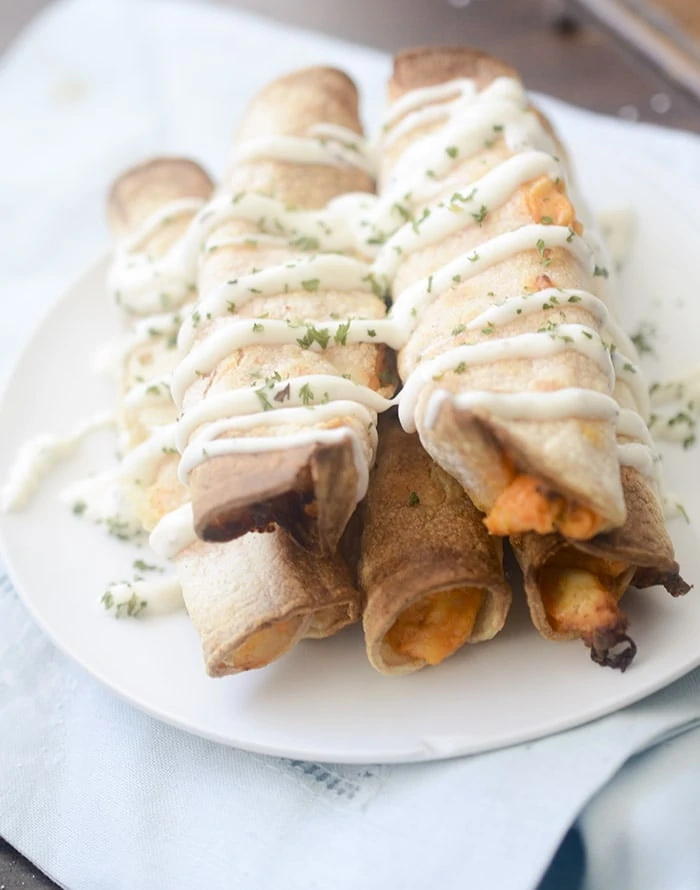 Stacked taquitos on a white plate with a sauce covering it.