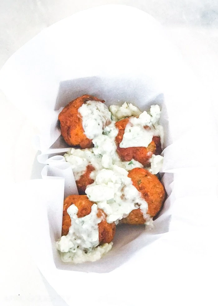 Chicken meatballs in a white container with a sauce covering it.