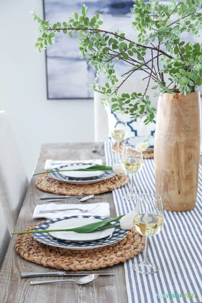 A simple Easter tablescape with gingham check plates, seagrass chargers, white tulips, and navy blue and white striped table runner.