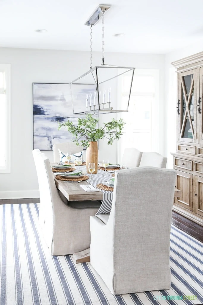 Spring and Easter dining room with large lantern pendant light, navy blue and white striped rug, linen dining chairs, reclaimed wood dining table and navy blue and white accents.