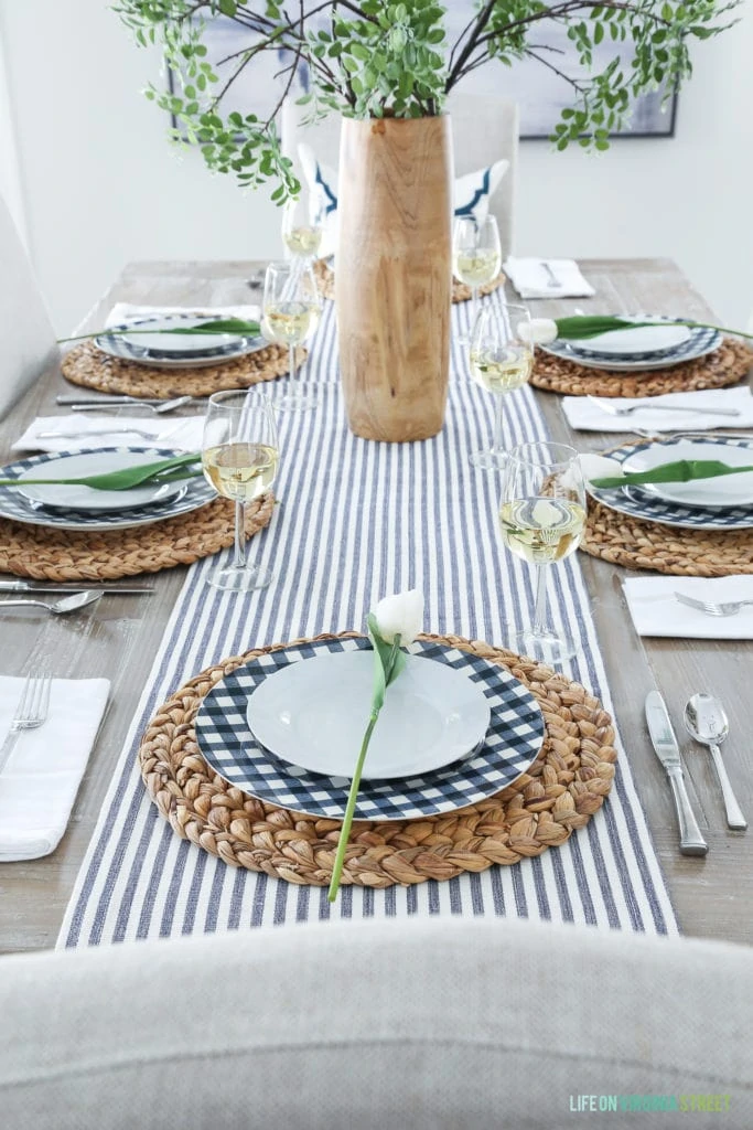 An Easter tablescape with a navy blue striped runner and navy and white gingham plates and a white rose on the plates.
