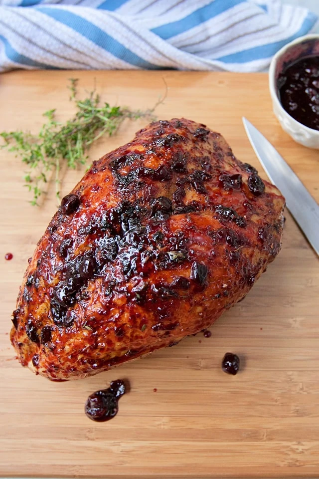Cherry glazed turkey on a wooden cutting board with a knife beside it.