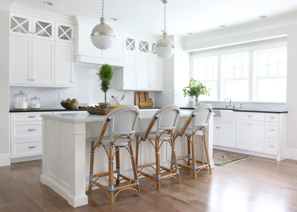A white kitchen island with wicker chairs.