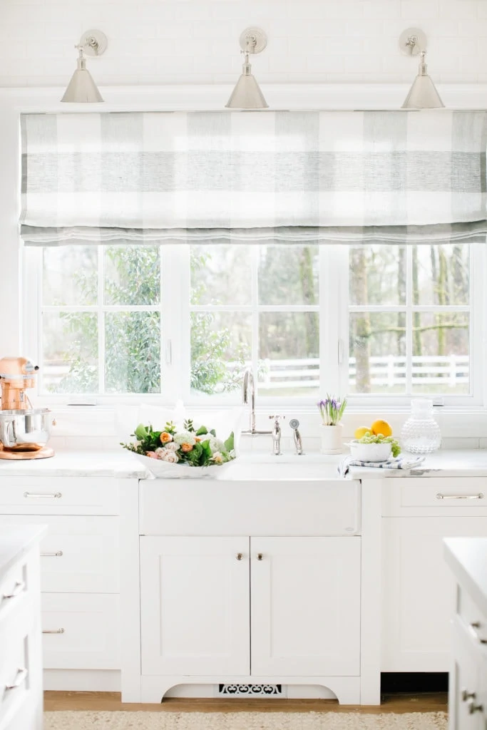 An all white kitchen with a bowl of flowers on the counter beside the sink.