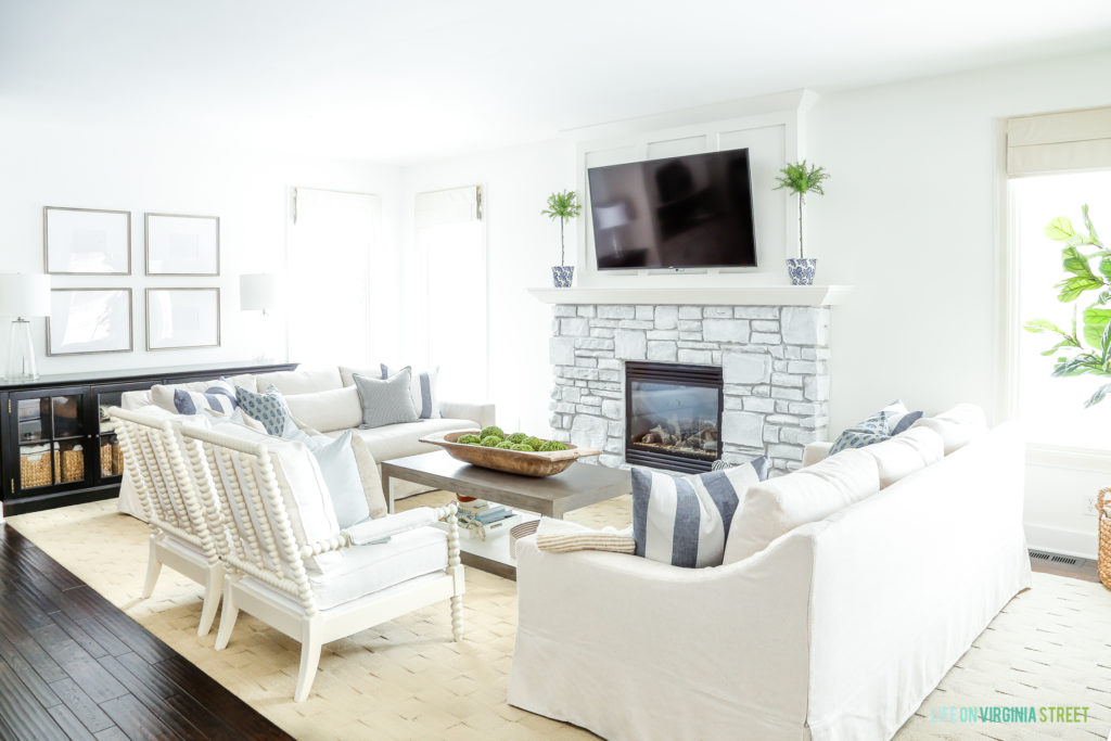 A whitewashed stone fireplace with a tv above it, white couches with blue and white striped pillows all in the living room.