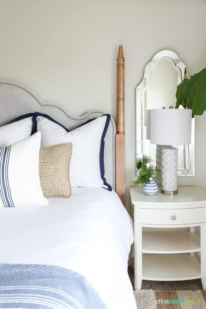 Off-white nightstands with an arched mirror and white textured lamp. White bedding is accented by blue and white striped pillows and a striped blanket.