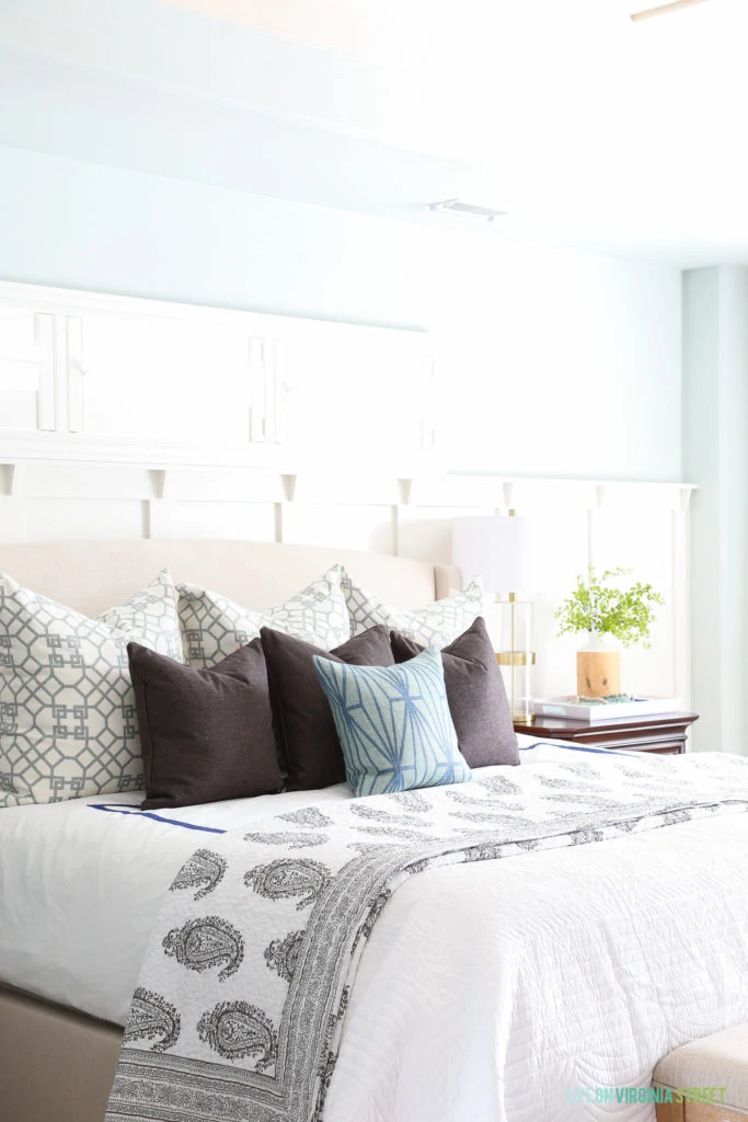 Tows of trellis pillows, and blue and green accents. Board and batten accent wall behind linen bed. 