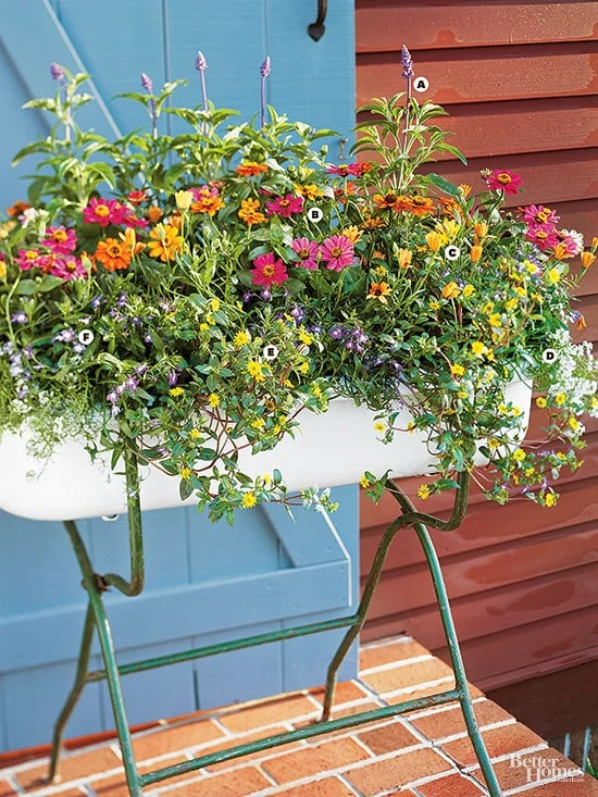 A planter on a stand filled with orange, purple and yellow flowers.