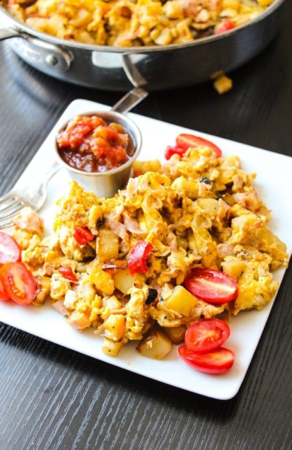 A scrambled egg skillet on a white plate with tomatoes.