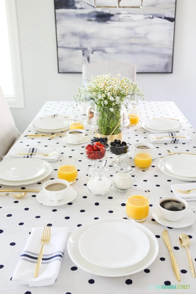 A brunch tablescape with a white and navy blue polka dot tablecloth and orange juice and coffee in cups.