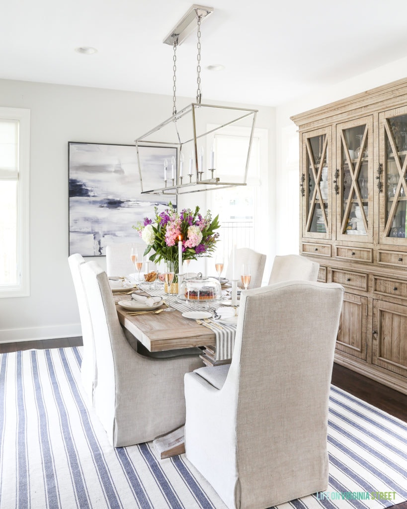 A wooden hutch, and pendant light all in the dining room with a blue and white striped rug.