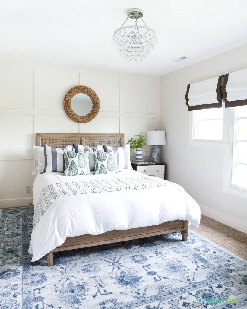 A queen sized bed in the guest bedroom, a neutral mirror above it and a chandelier over the bed.