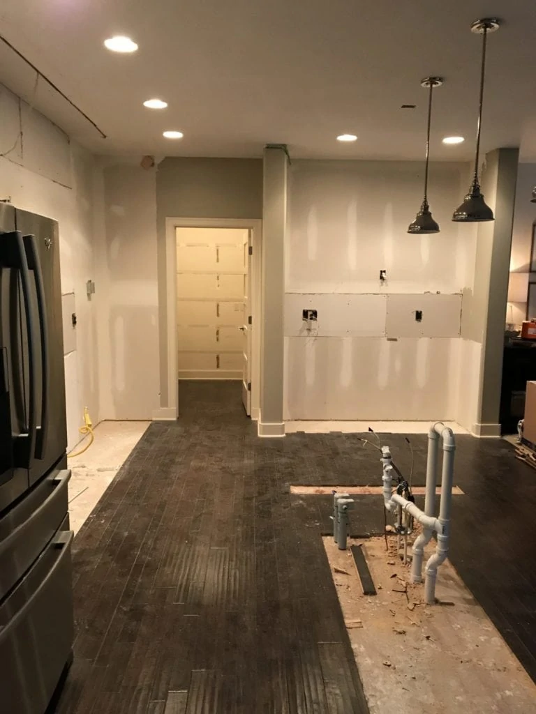 The empty kitchen with pot lights and hanging lights but no cabinets in the kitchen.