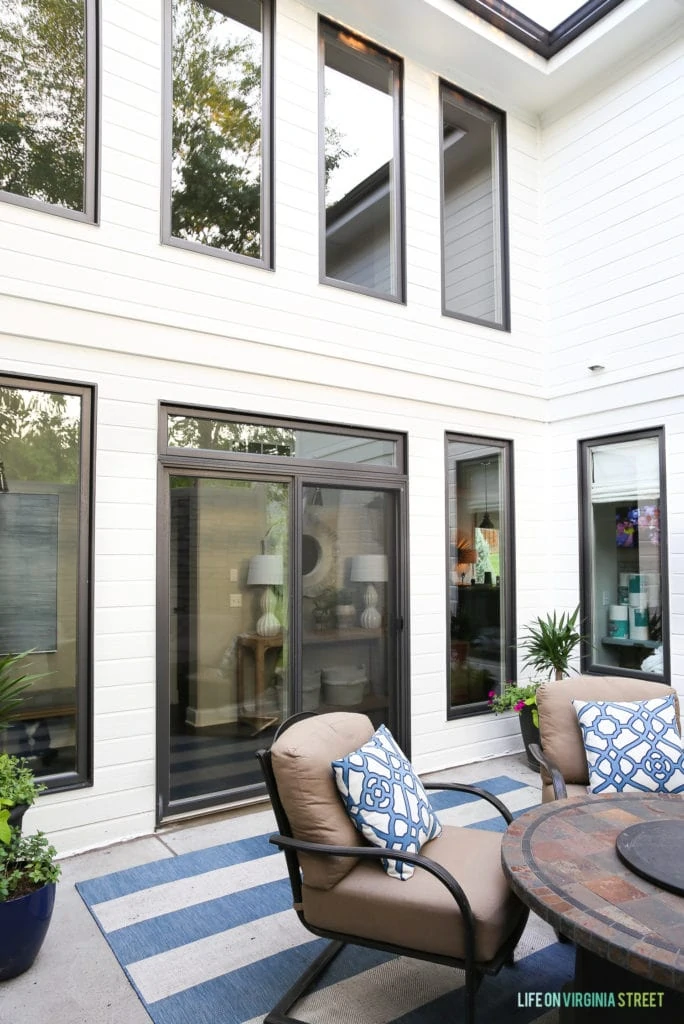 The back patio of the house with a round table and chairs and a blue striped rug on the patio.