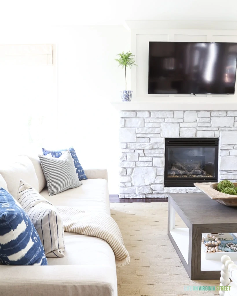 Blue and white coastal living room with shibori and striped pillows. Painted stone fireplace with a white-wash look.