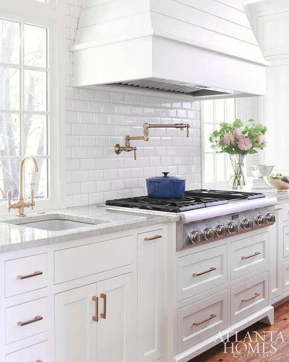 A white kitchen with flowers on the counter and gold/brass pulls.