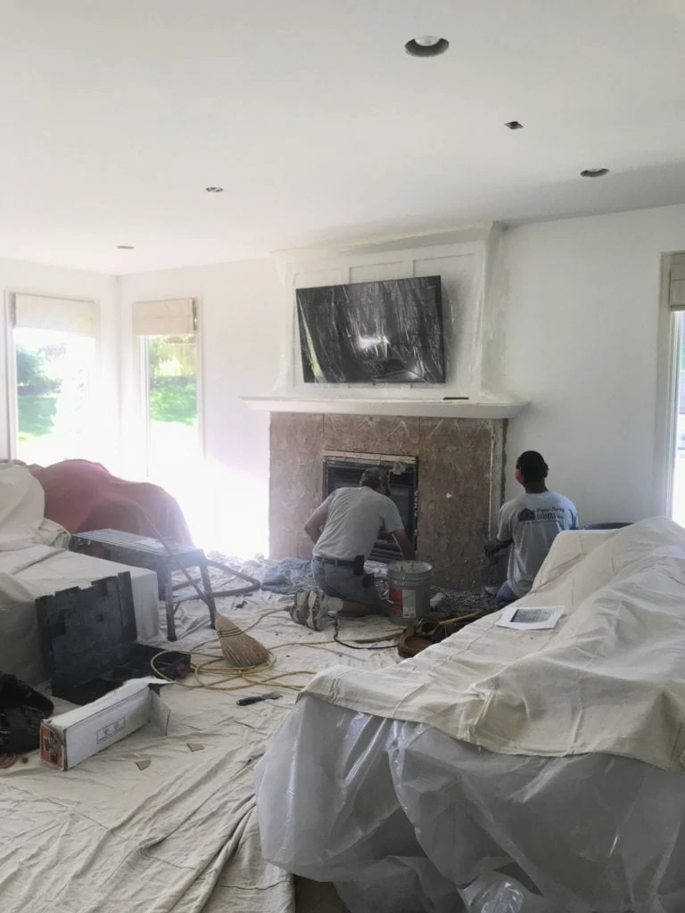 Living room with drop cloth protecting the furniture and two men working on the fireplace.