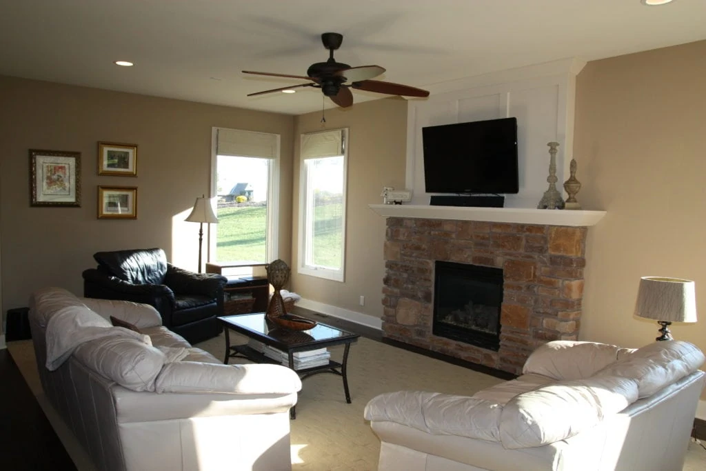 Dark stone fireplace in living room with beige walls and ceiling fan.