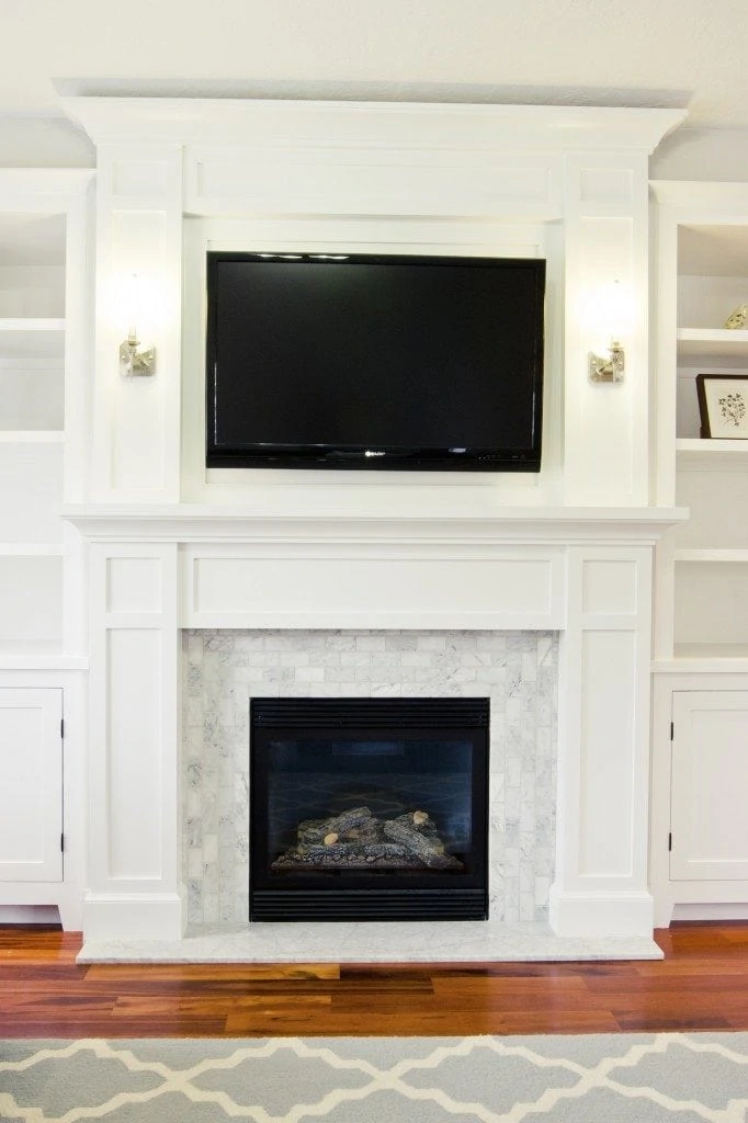 Wooden floor with grey rug and white fireplace with black TV on top of it.