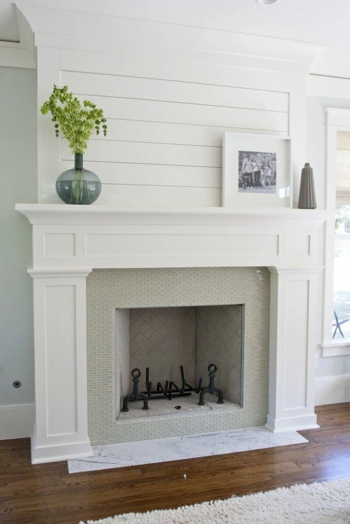 White neutral fireplace with vase on top filled with greenery and family picture on mantel.