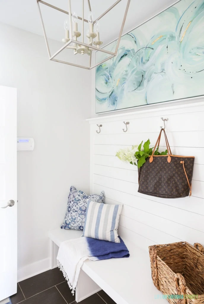 A mudroom makeover with pale gray walls, white shiplap wall with hooks, and blue, white and aqua accents. Love the open lantern light fixture.