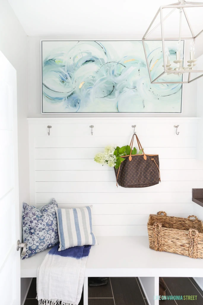 A coastal inspired mudroom makeover with white shiplap, aqua abstract art, a Darlana pendant knock-off lantern, and blue and white accents.