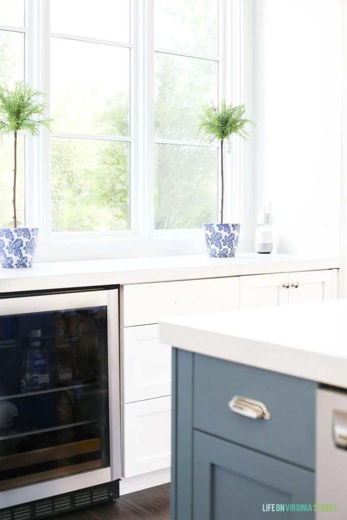 White kitchen with a blue island and topiaries in a blue and white ceramic pot. Google Home blends in perfectly in the space.