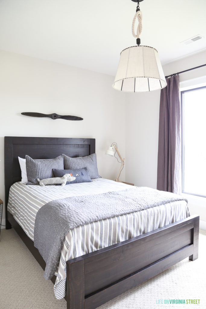A darker framed bed with headboard, purple curtains and a white light fixture above the bed in the boys room.