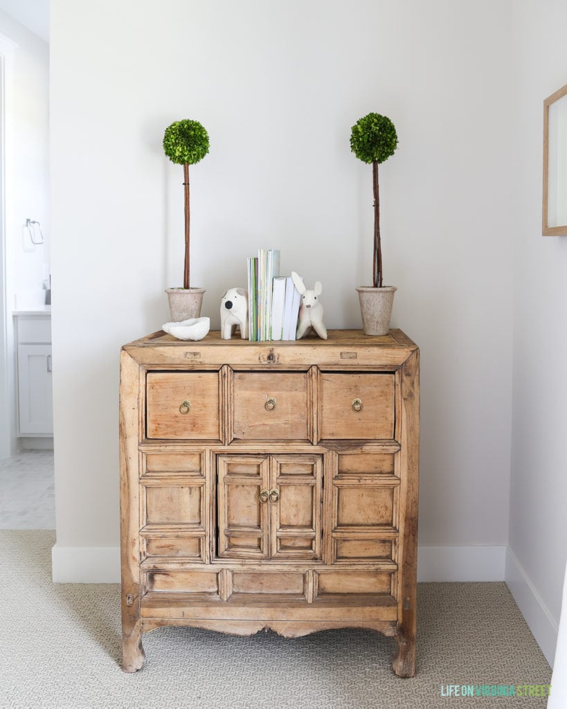 Wooden dresser with green topiary on top.