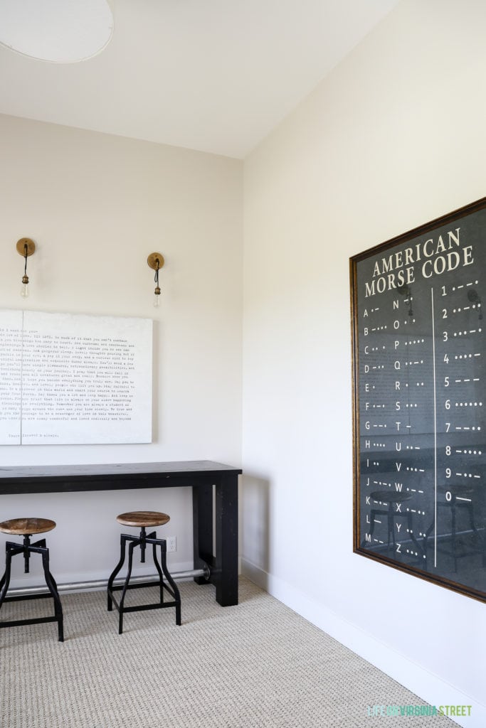 A desk and chairs in the room with a picture of the morse code on the wall.