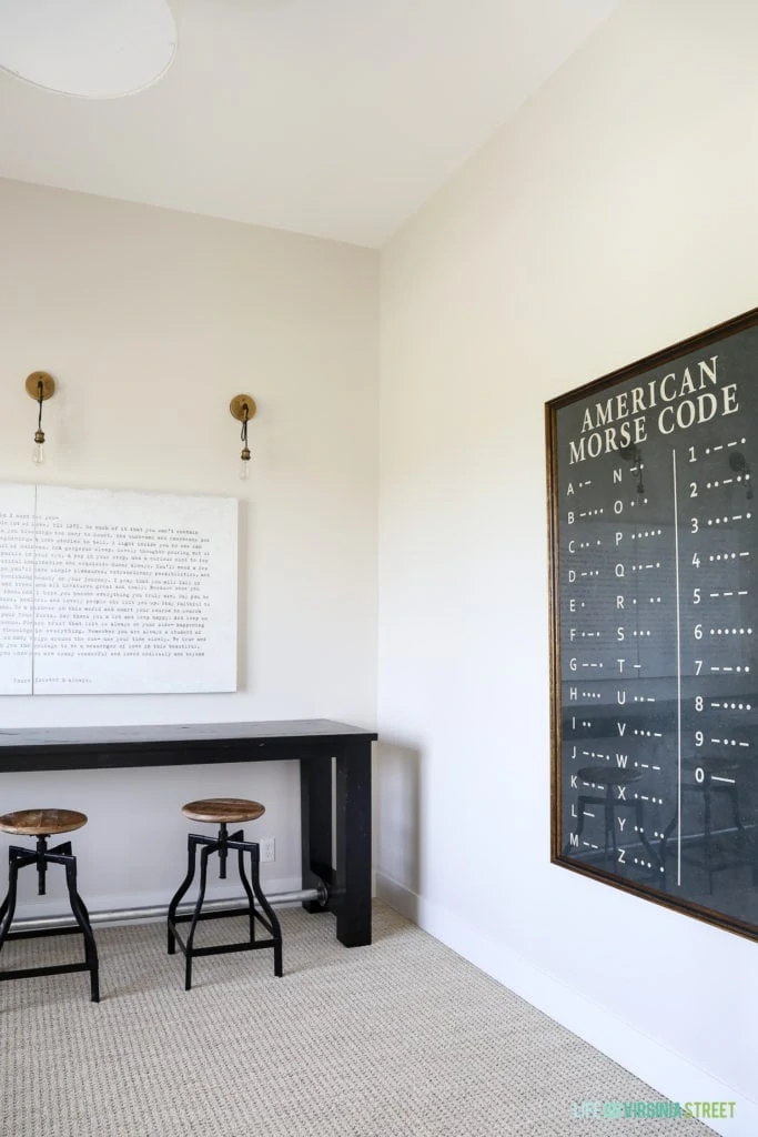 A desk and chairs in the room with a picture of the morse code on the wall.