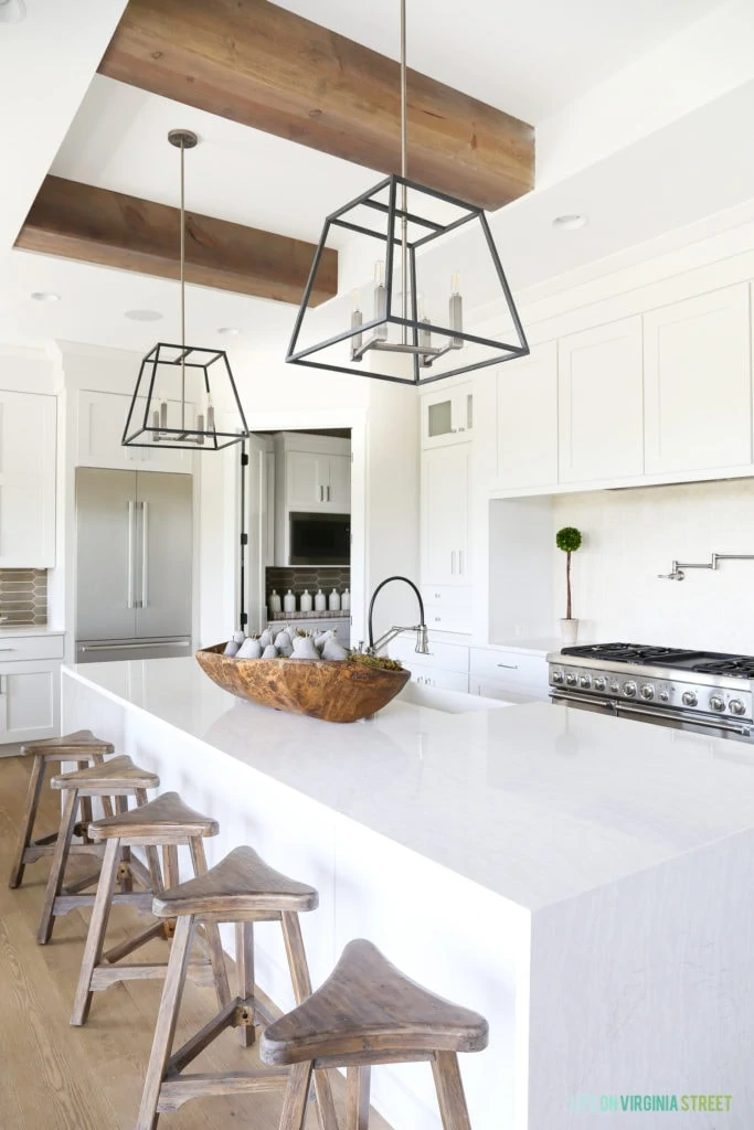 A California modern farmhouse kitchen with waterfall island and wood barstools. I love the natural wood beams on the ceiling and the industrial metal light pendants.