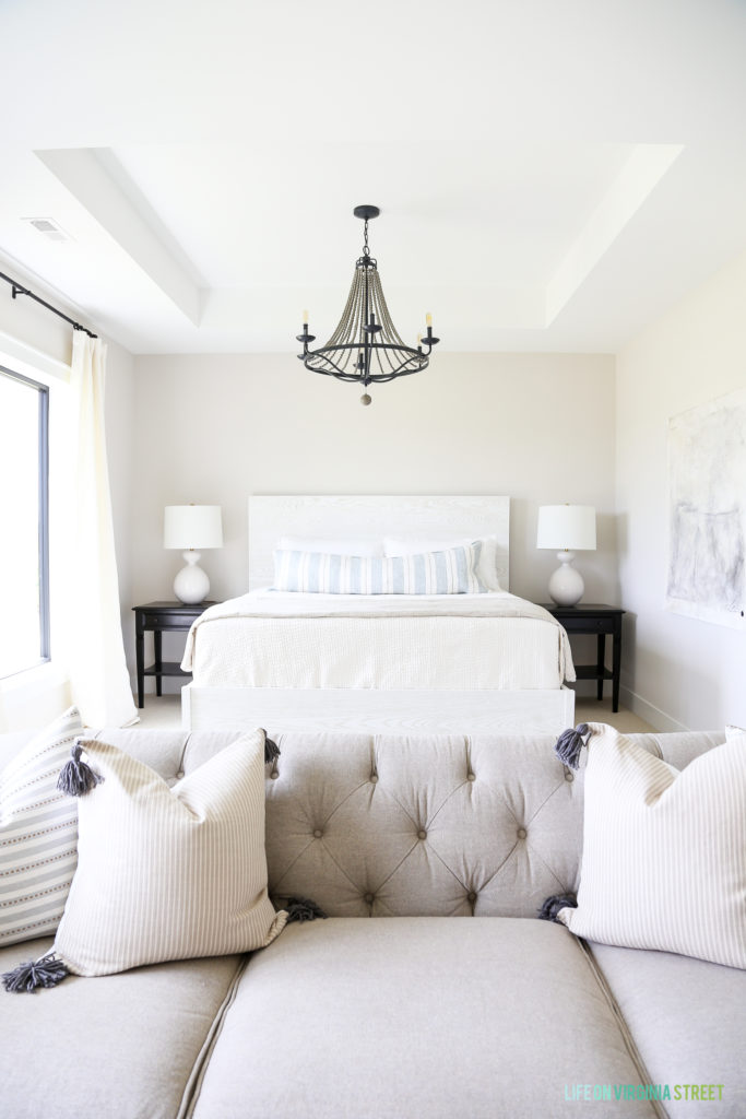 A white bed, neutral couch and a black chandelier in master bedroom.