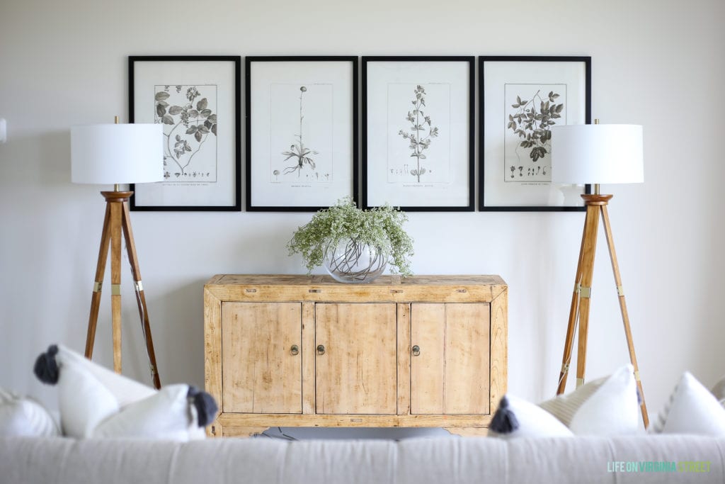 Four pictures on the wall in black frames, flanked by two floor lamps and a wooden cabinet in between them.