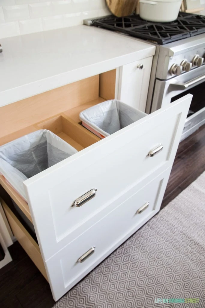 Custom pull-out garbage can drawer in a white coastal kitchen. Built by McClain's Custom Cabinets.