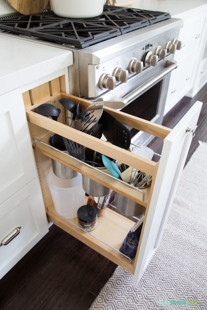 White kitchen cabinets with a pull-out rack for utensils.