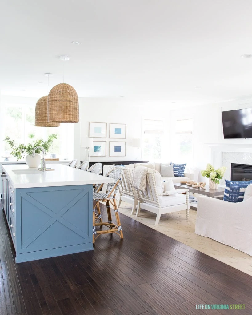 Blue kitchen island, woven pendant light fixtures, and neutral living room and blue, green and white accents.