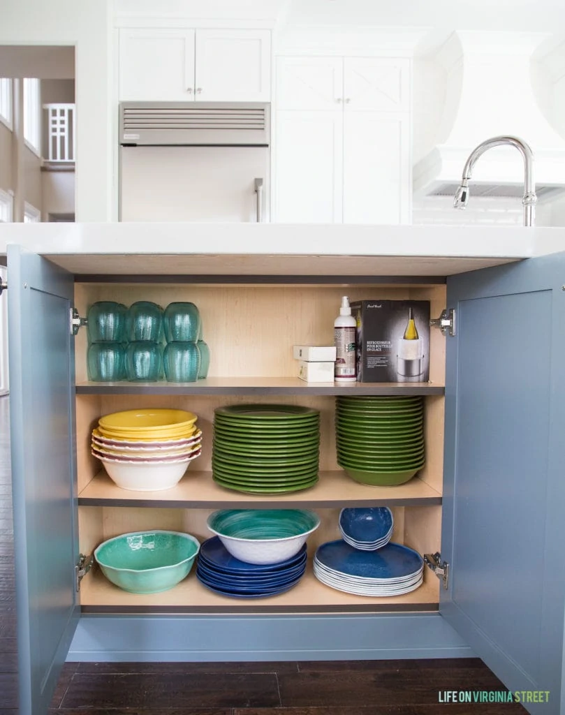 Kitchen island door that are opened with plates and glasses inside.