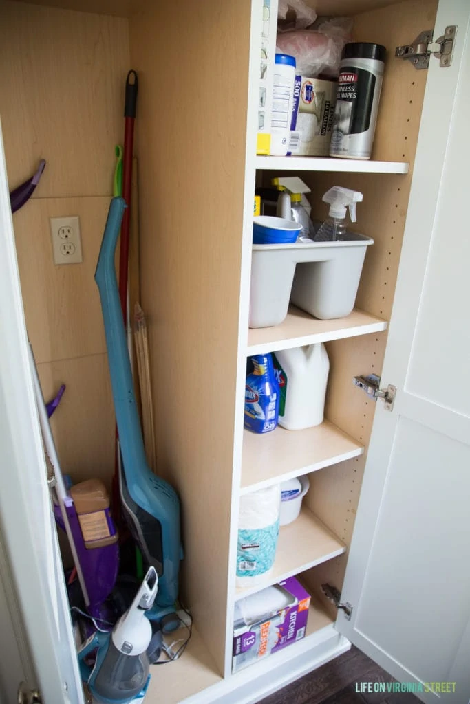A kitchen closet with cleaning supplies inside.