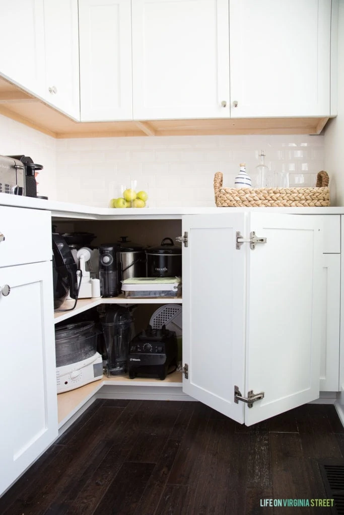 White kitchen cabinets with one corner door opened to reveal appliances inside.