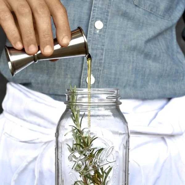 Pouring a shot into a mason jar with a sprig of greenery.