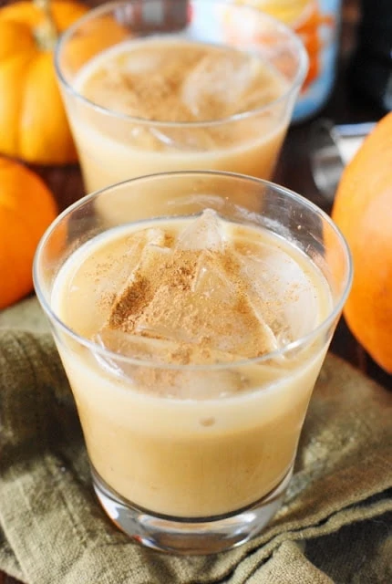 Two glasses of white Russian with pumpkin in it and pumpkins around it.