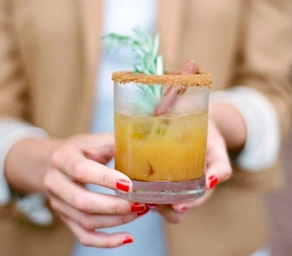 Woman holding an apple cider cocktail that has a heavily sugared rim.