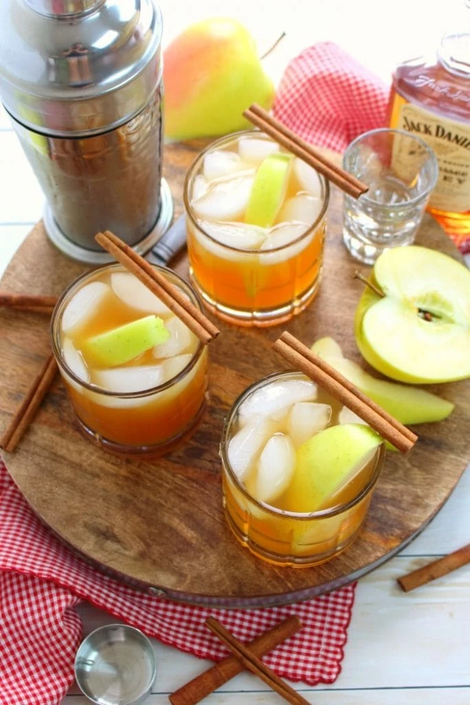 Three glasses of apple cider whiskey with a cinnamon stick on top.